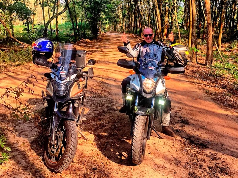 Two riders on red dirt trails through the jungle