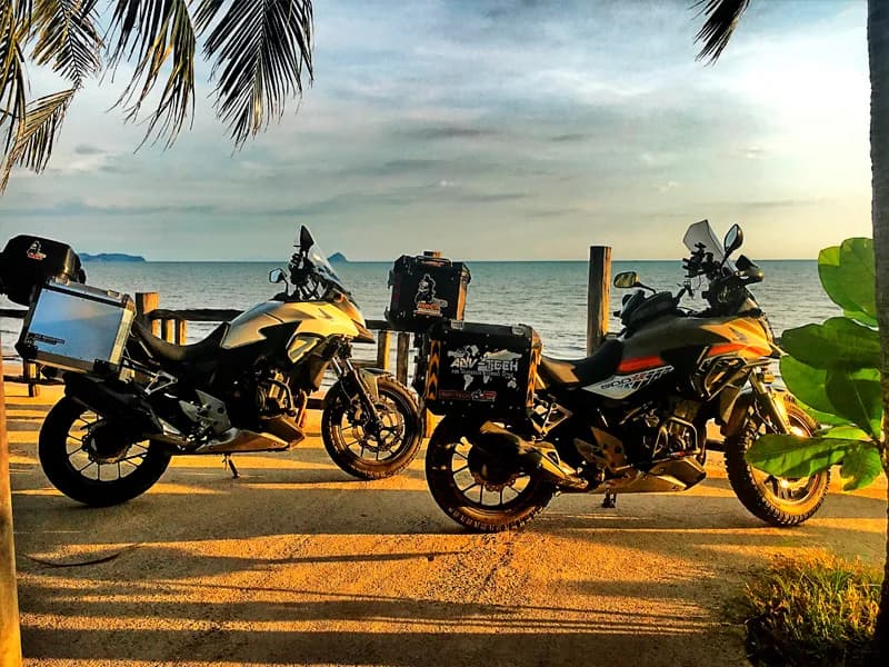 Three adventure bikes parked beachside at sunset